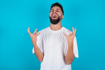bearded caucasian man wearing white T-shirt over blue background crying and screaming. Human emotions, facial expression concept. Screaming, hate, rage.