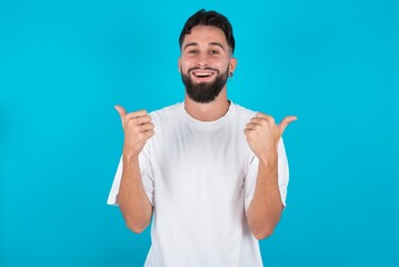 Fototapeta premium Optimistic bearded caucasian man wearing white T-shirt over blue background showing thumbs up with positive emotions. Quality and recommendation concept.