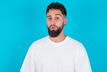 Obraz premium bearded caucasian man wearing white T-shirt over blue background expressing disgust, unwillingness, disregard having tensive look frowning face, looking indignant with something.