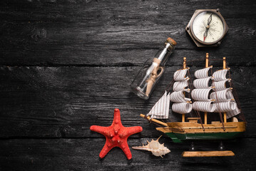 Pirate background. Message in the bottle, compass, starfish and ship on the black wooden table flat...