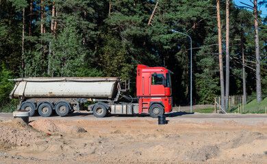 Heavy truck with trailer and bulk cargo - soil, gravel, sand driving next to forest