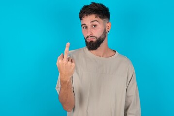 bearded caucasian man wearing casual T-shirt over blue background shows middle finger bad sign asks...