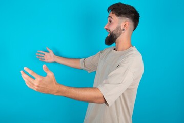 Funny astonished bearded caucasian man wearing casual T-shirt over blue background look empty space...