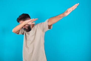 Photo of funky bearded caucasian man wearing casual T-shirt over blue background show disco move dab