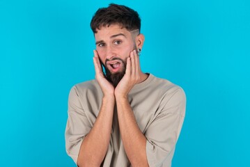 Obraz premium Upset bearded caucasian man wearing casual T-shirt over blue background touching face with two hands