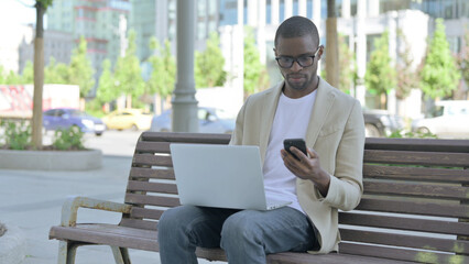 African Man Using Smartphone and Laptop while Sitting Outdoor on Bench