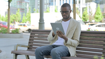 African Man using Tablet while Sitting Outdoor on Bench