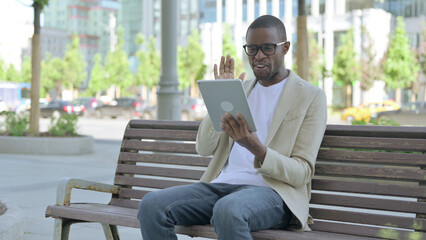 Fototapeta premium Online Video Chat on Tablet by African Man Sitting Outdoor on Bench