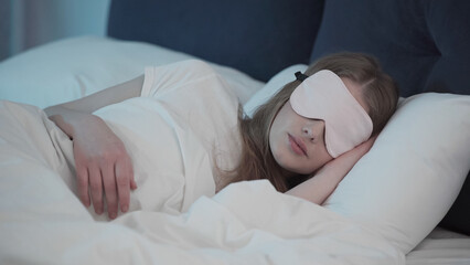 Young woman in sleep mask lying on bed at night.