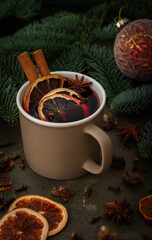 Obraz na płótnie Canvas Christmas hot alcoholic drink mulled wine in a mug with citruses, aromatic spices and cinnamon among the spruce branches