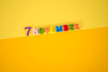 November 7 on a yellow, paper background with multicolored and wooden letters with space for text.