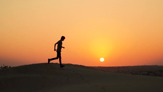 Slow motion silhouette shot of an Indian man running on the top of the sand dunes of Thar desert in front of the sun during the sunrise at Sam sand dunes in Jaisalmer, Rajasthan, India.