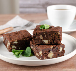 Chocolate homemade brownies with dried cranberries and walnuts on the white  plate with a cup of black tea