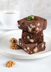 Chocolate homemade brownies with dried cranberries and walnuts on the white  plate with a cup of black tea