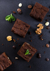 Chocolate homemade brownies with mint, walnuts and chocolate drops on the black background. Top view or flatlay.