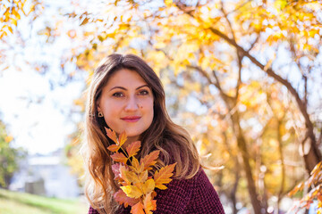 Beautiful woman in burgundy sweater on a background of autumn tree.