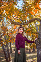 Portrait of beautiful woman in burgundy sweater on a background of autumn tree.	
