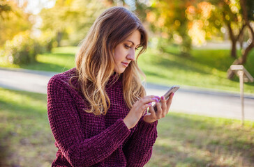 Young woman using the mobile smart phone. Autumn park walking outdoors.