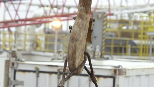 Metal hook lifts metal ropes. Close-up. White container behind in a blur