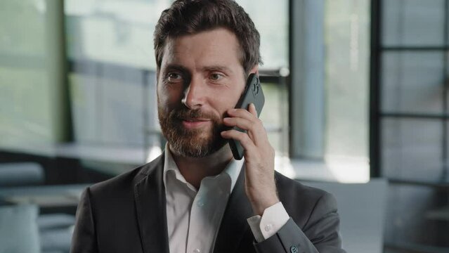 Emotional adult bearded professional businessman client Caucasian man making business call talking on phone in office close up salesman enjoying mobile conversation indoors distant talk negotiation