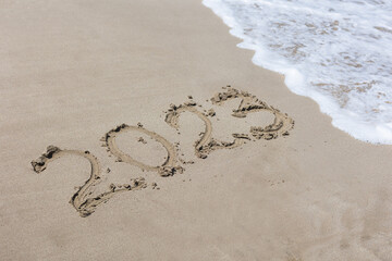 Handwriting new year numbers 2023 on the sand in the summer at sea, which will soon be washed away by the approaching wave