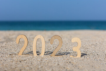 Wooden new year numbers 2023 on the sand in the summer at beautiful sea. Flat lay, top view, christmas card
