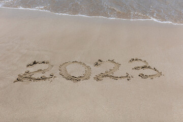 Painted new year numbers 2023 on the sand in the summer at sea, which will soon be washed away by the approaching wave