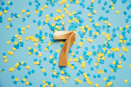 Number 7 seven golden celebration birthday candle on yellow and blue confetti Background. seven years birthday. concept of celebrating birthday, anniversary, important date, holiday
