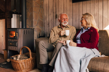 Smiling mature lovers, sitting on the sofa, holding cups of coffee.