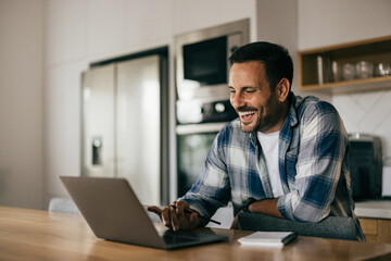 Businessmen working online, from the home, smiling and looking at laptop.