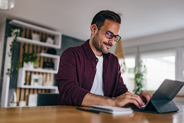 Obraz premium Adult man working over the tablet, typing something on the keyboard.