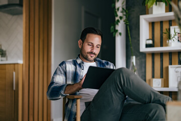A serious-looking man spending time indoors, at home, using modern technology.