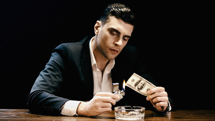 Businessman burning dollar banknote near ashtray isolated on black.