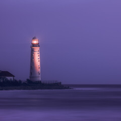 A lighthouse on the coast of the sea at dusk, its bright lamp is a landmark for ships. Seascape, nature background.