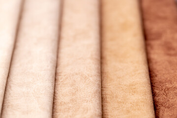 Fabric swatches in different colors are stacked for selection. A variety of shades of upholstery material for furniture and interior. Fabric texture close up. A set of multi-colored rolls of material.