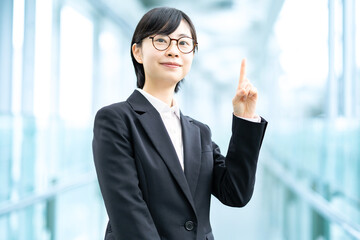 人差し指を上げたポーズをするスーツ姿の若い女性