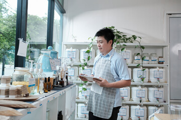 Asian male shopkeeper checks stock of natural organic products at window display in refill store, zero-waste and plastic-free grocery, eco environment-friendly, sustainable lifestyles, reusable shop.