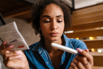 Young black woman holding pregnancy test and instruction at home - obrazy, fototapety, plakaty