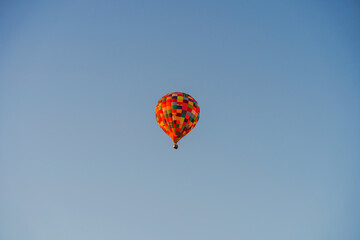 A colorful balloon with tourists flies across the blue sky
