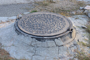 one black metal sewer hatch lies in gray concrete on the street