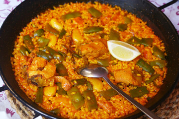 spanish paella close up photo in frying pan with shrimps, peas and lemon slice