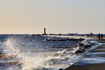 Pier, moll to the lighthouse covered with waves' splashes. Selective focus - obrazy, fototapety, plakaty