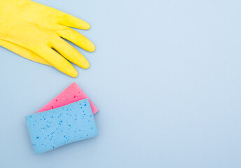 Blue and pink kitchen sponges with yellow rubber glove on blue with copy space