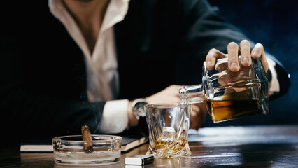 Cropped view of businessman pouring whiskey near cigar and lighter on black.