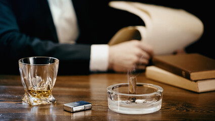 Cropped view of cigar and whiskey near blurred businessman isolated on black.