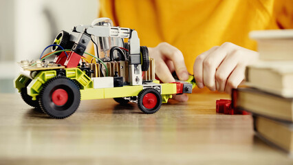 cropped view of child playing with electric car made of building blocks on table near books.
