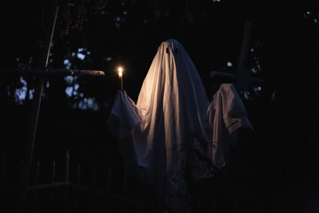 Ghost holding candle in the cemetery between graves during Halloween at night