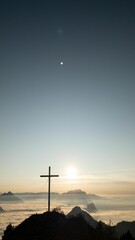 Vertical shot of the silhouette of a cross on top of the hill against the sunrise background