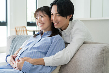 Fototapeta premium 自宅で笑顔でお腹をさする日本人妻と後ろからハグをする夫