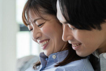 自宅で笑顔でお腹をさする日本人妻と後ろからハグをする夫